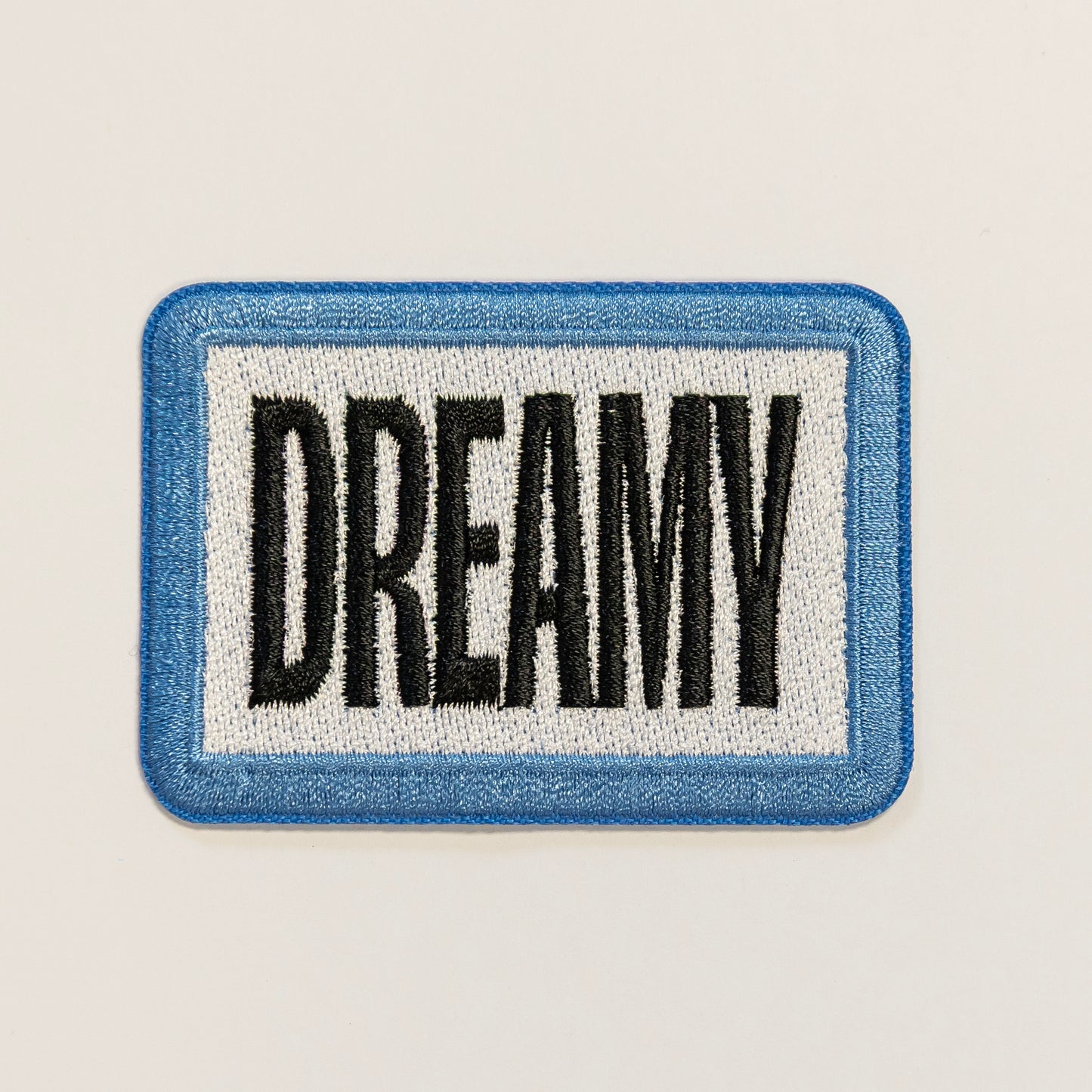 Rectangular patch with a blue border and white background, featuring the word "DREAMY" in bold black letters.