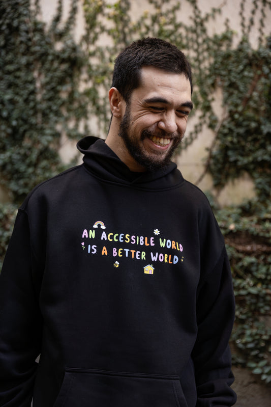 Will wears a black hoodie with colourful text which reads "An accessible world is a better world". The design has small designs around it including flowers, a rainbow, a bee, a house and a star.