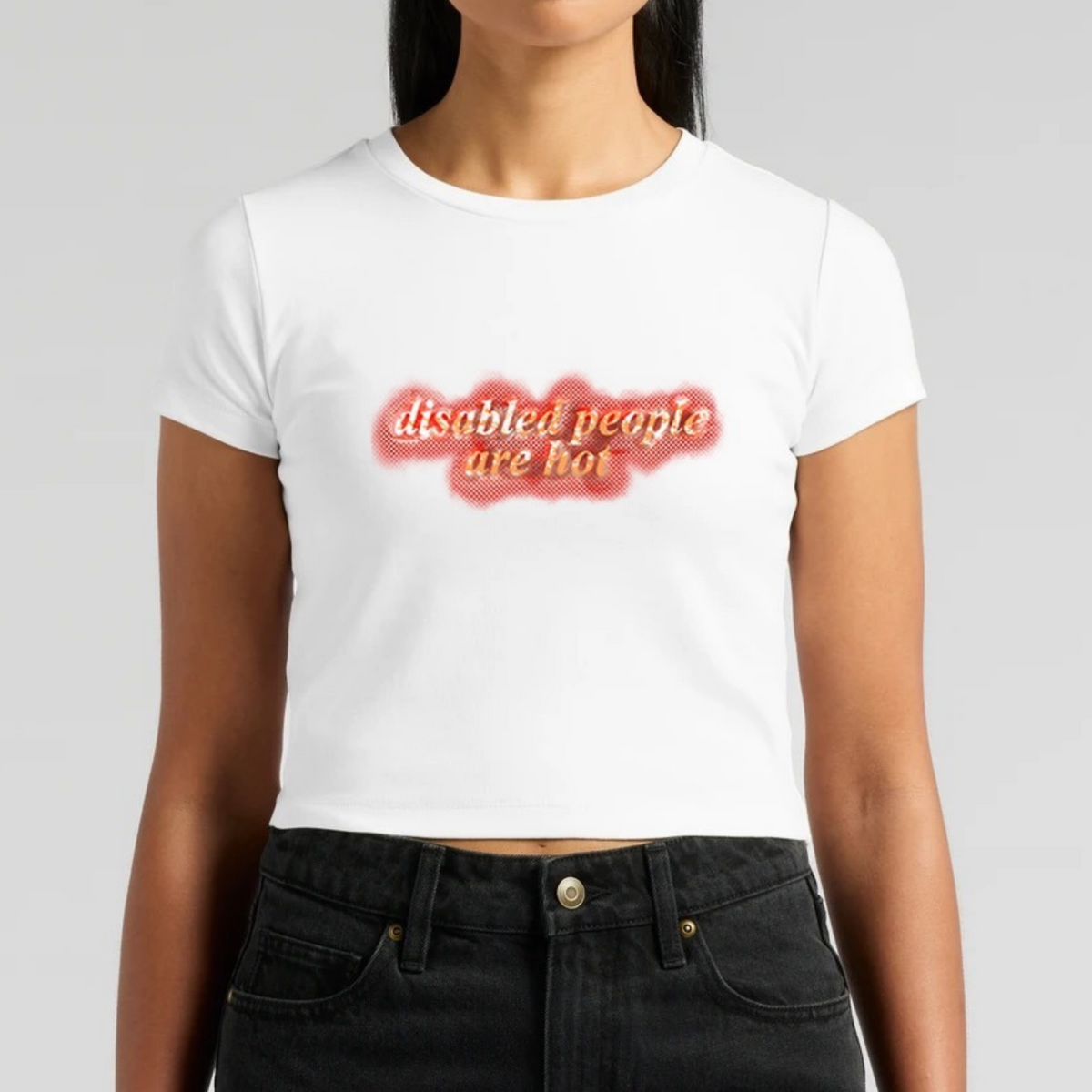 A white mini T-shirt printed with the words “disabled people are hot” in gold lettering over a red halftone shape.
