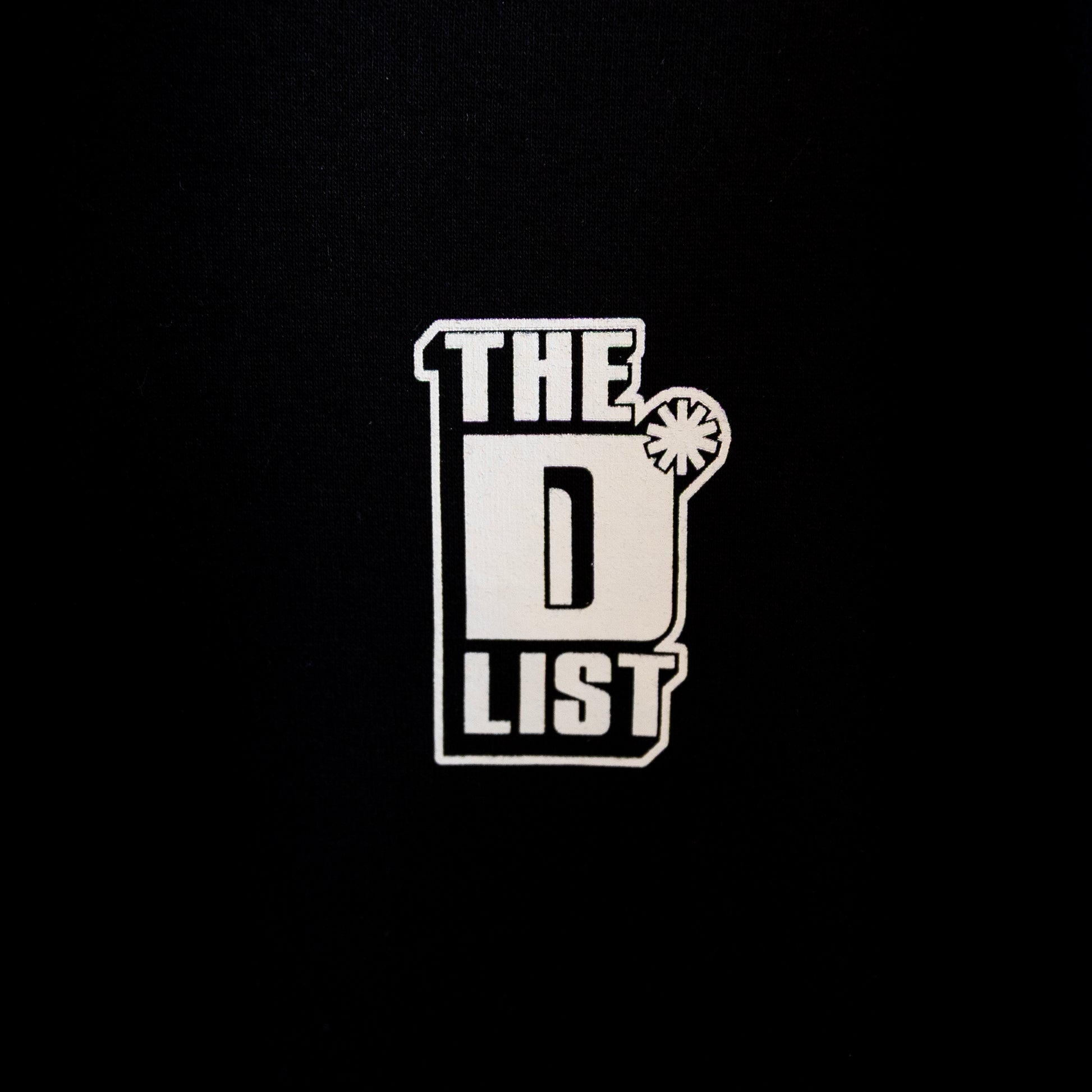 Close up of the white "The D*List" logo print on the black left chest area of the hoodie