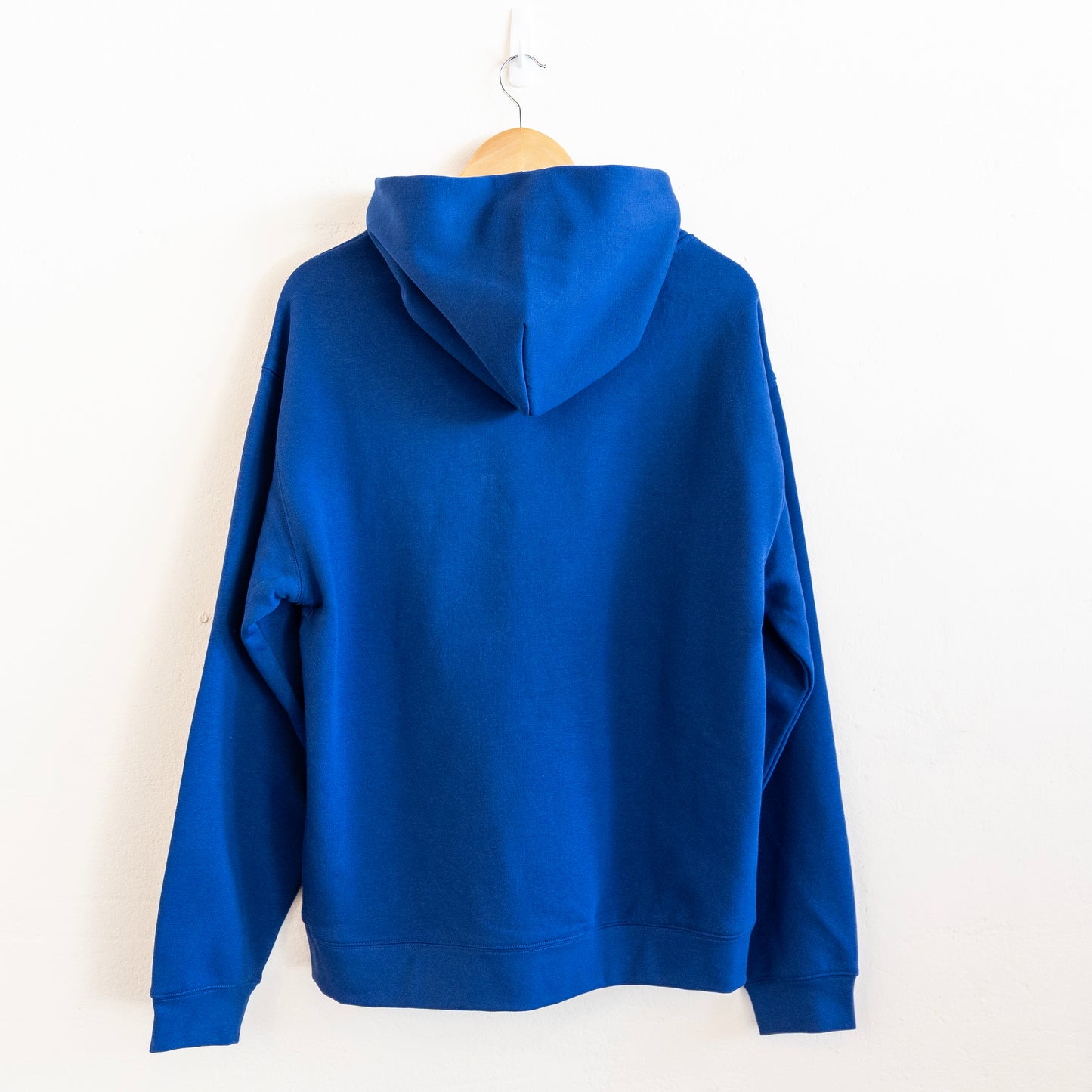 The back of a blue hoodie hung up against a white wall.