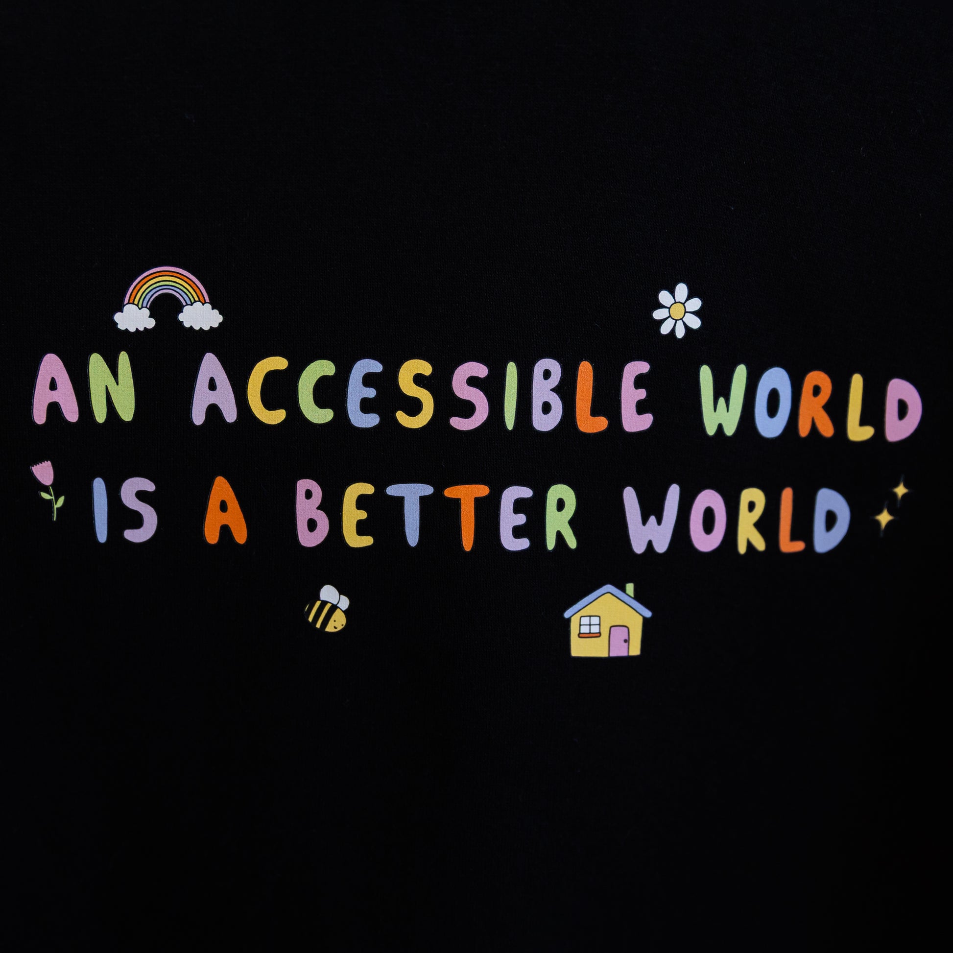 Close up of the black hoodie with a print of colourful text which reads "An accessible world is a better world". The design has small designs around it including flowers, a rainbow, a bee, a house and a star.