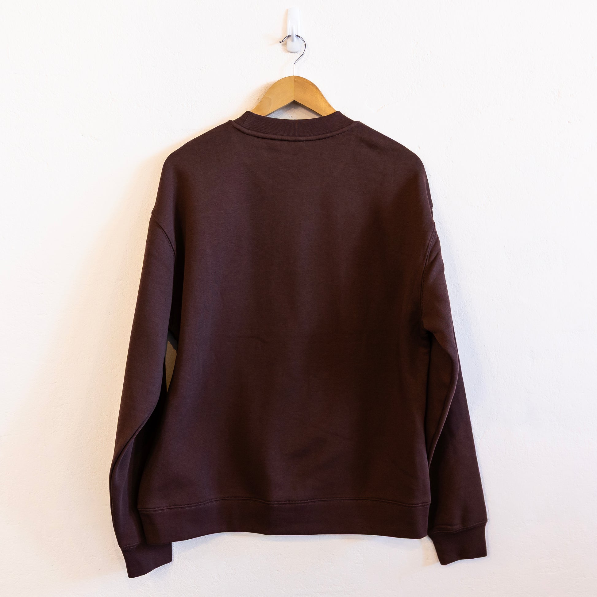 The back of a brown sweatshirt on a hanger against a white wall.