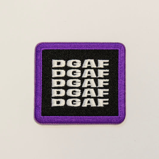 A square patch with a purple border and black background features the bold white letters "DGAF" repeated in five rows, conveying a casual, defiant tone.