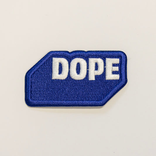 Blue embroidered patch with the word "DOPE" in bold white letters. The patch is shaped as if to mimic a three-dimensional rectangle.