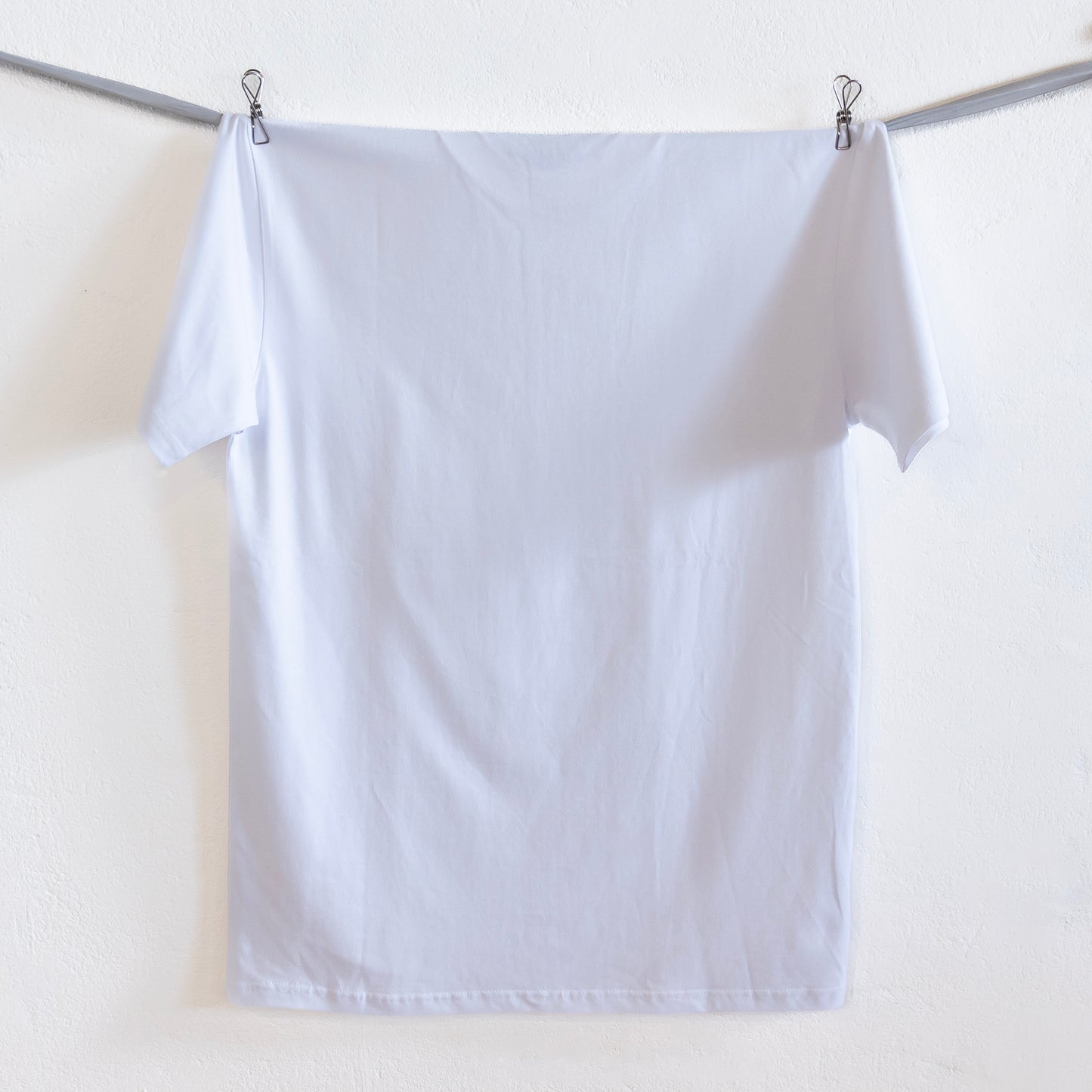 The back of a white t-shirt hangs on a grey ribbon against a white wall