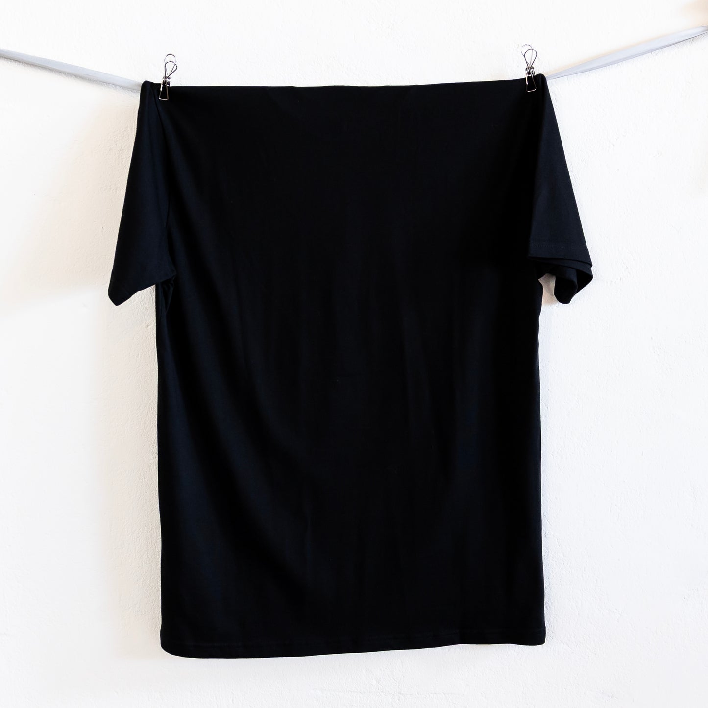 Black t-shirt hanging on a silver ribbon against a white background