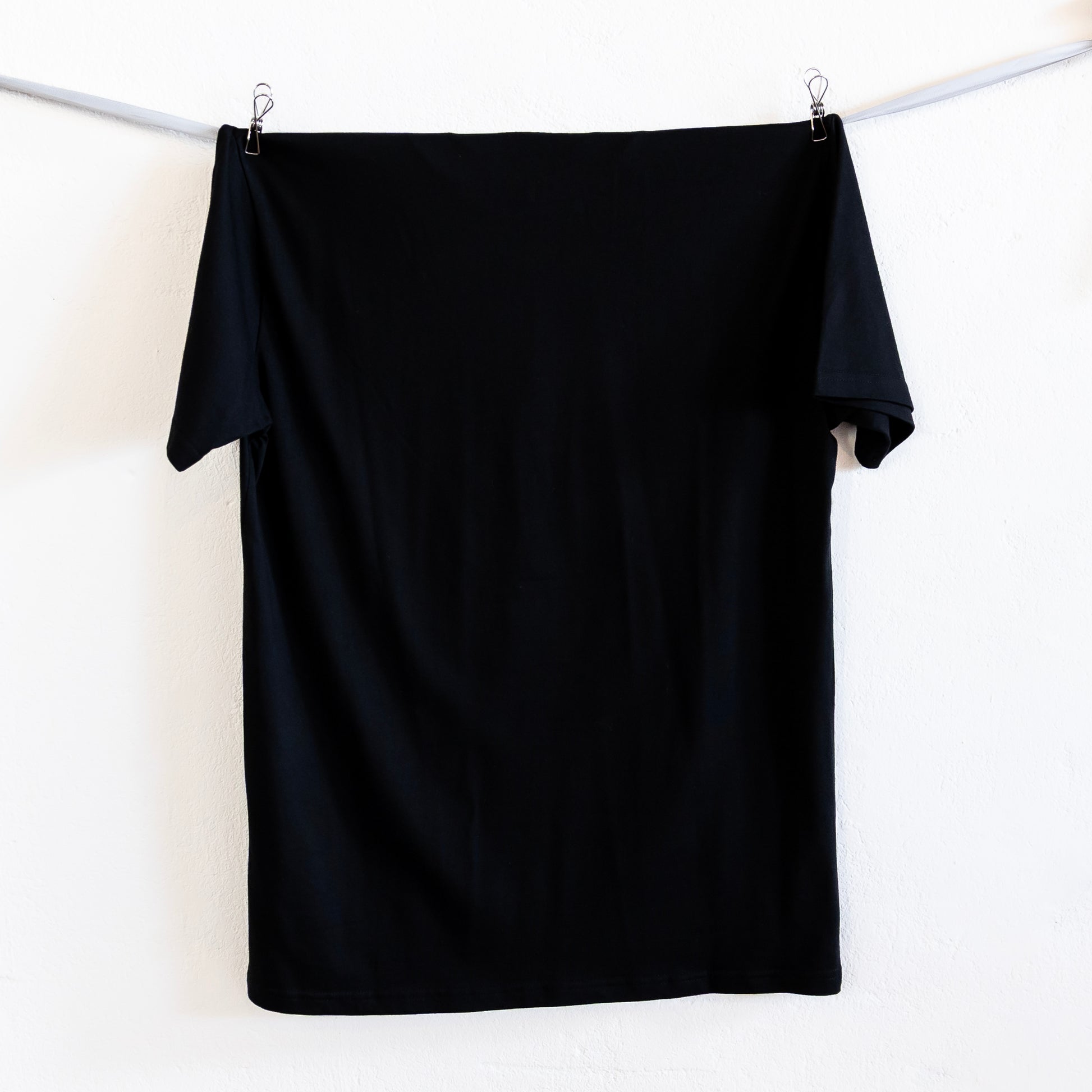 Black t-shirt hanging on a silver ribbon against a white background