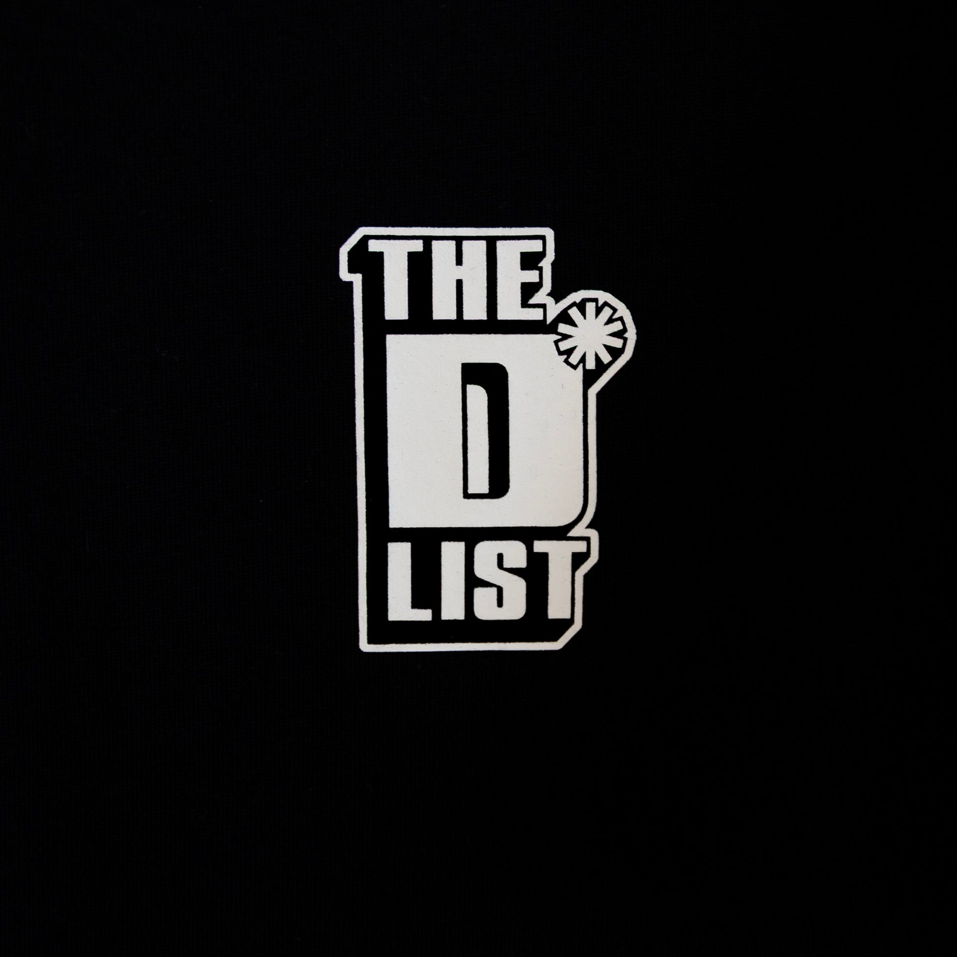 Close up of the white "The D*List" logo print on the black left chest area of the tee