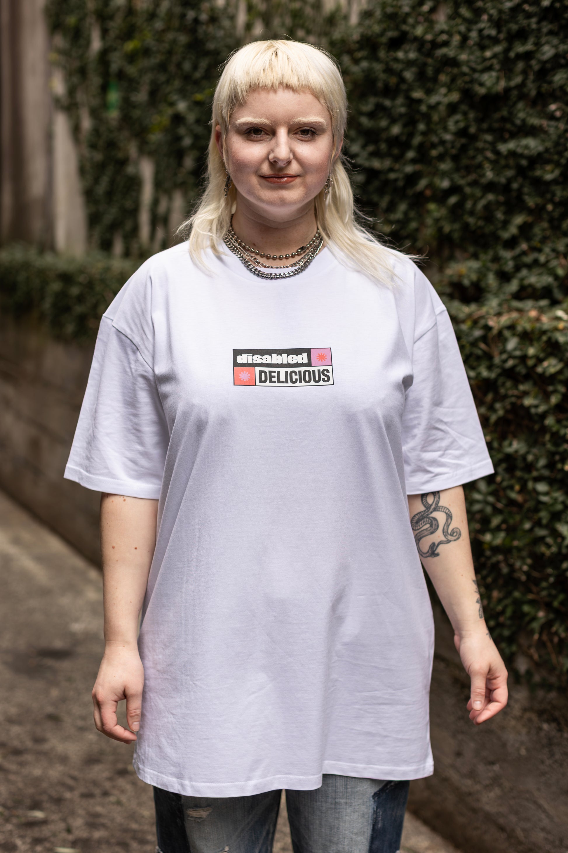 Von wearing a white T-shirt that reads "disabled DELICIOUS." The design features two tohuwhetū and is in pink, red, black and white.
