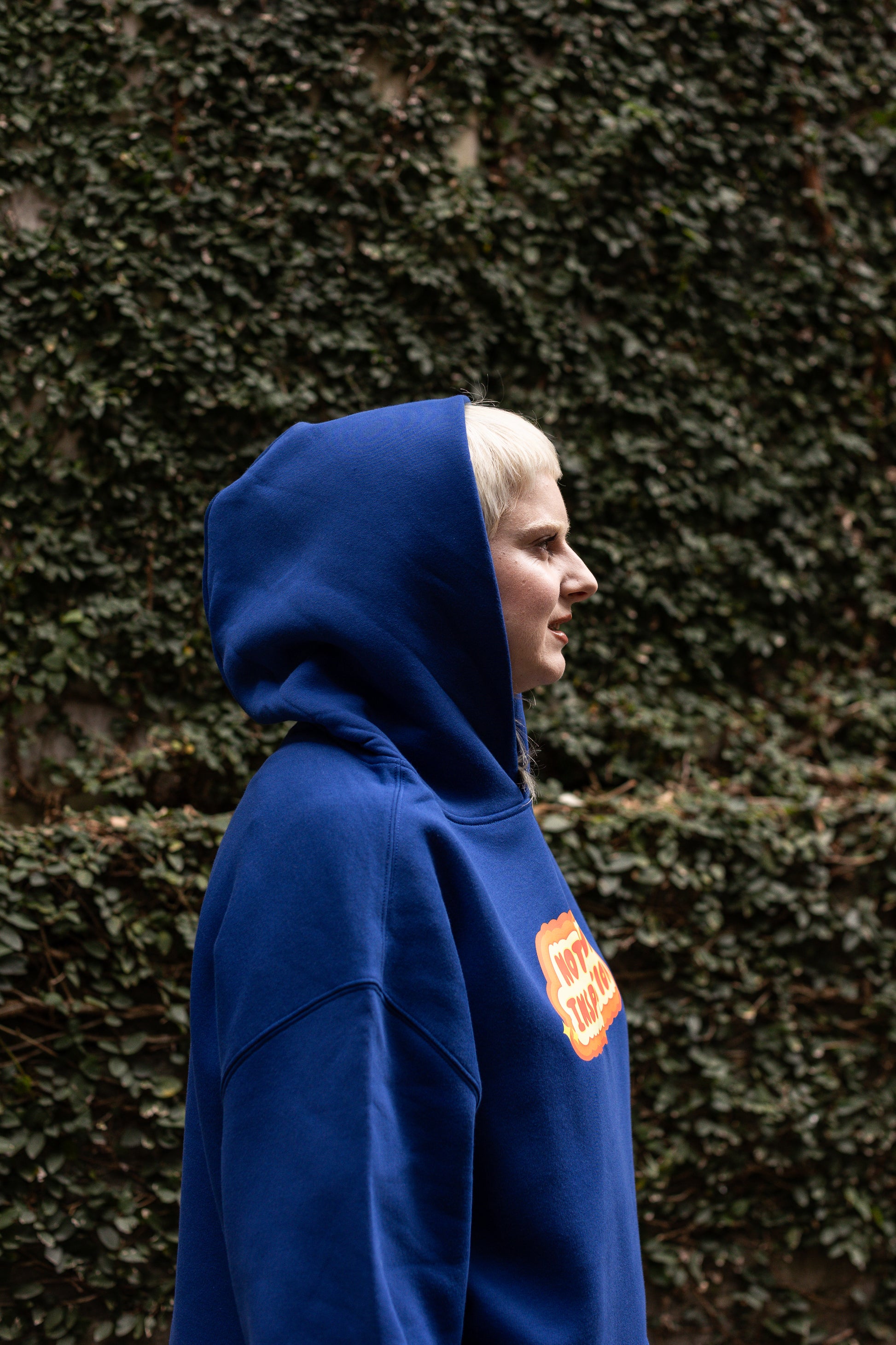 Von, facing the right, wearing a blue hoodie the hood up, against a textured wall