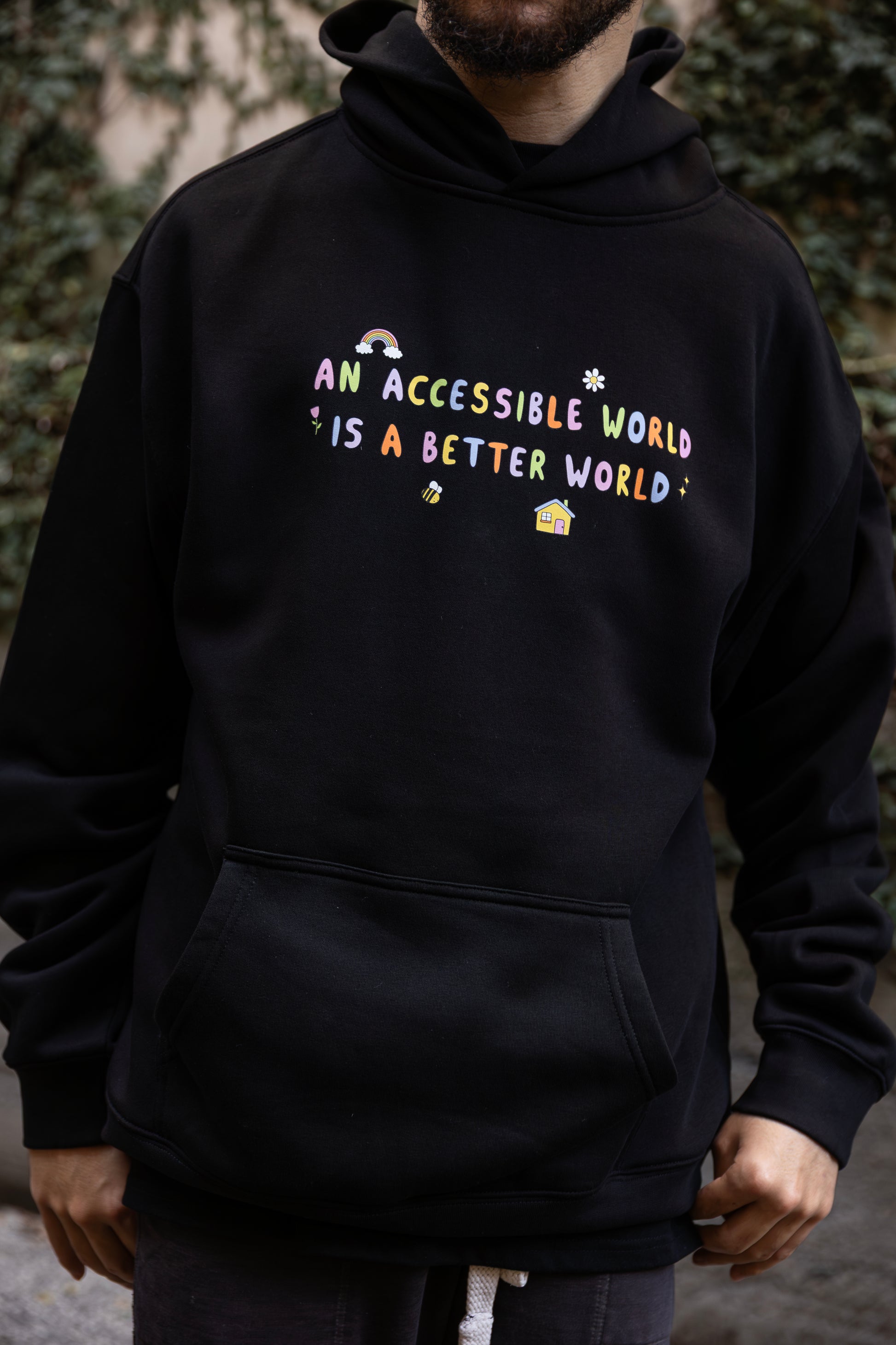 Will wears a black hoodie with colourful text which reads "An accessible world is a better world". The design has small designs around it including flowers, a rainbow, a bee, a house and a star.