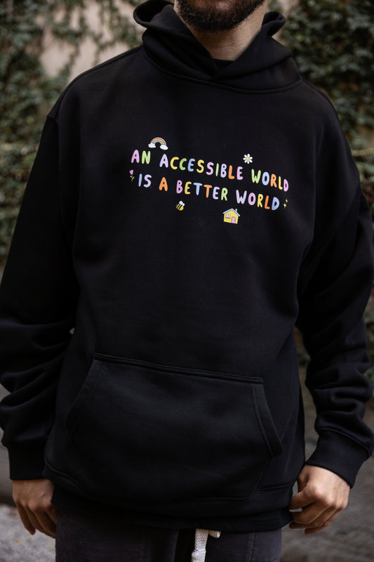 Will wears a black hoodie with colourful text which reads "An accessible world is a better world". The design has small designs around it including flowers, a rainbow, a bee, a house and a star.