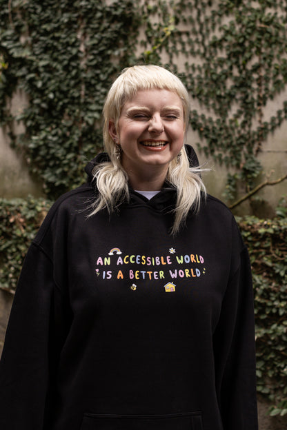 Von wears a black hoodie with colourful text which reads "An accessible world is a better world". The design has small designs around it including flowers, a rainbow, a bee, a house and a star.